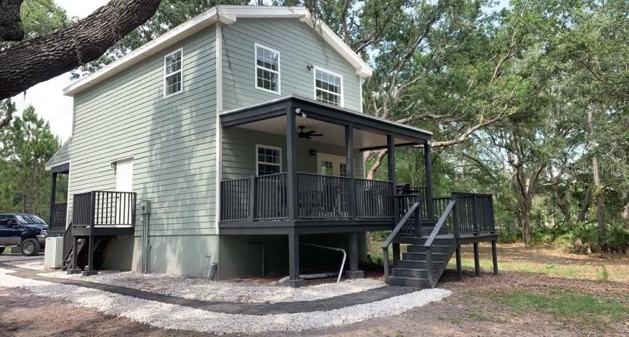 A two-story light green house features a dark-colored elevated deck and a gravel path — 7152 SANDY LANE, WESLEY CHAPEL, FL