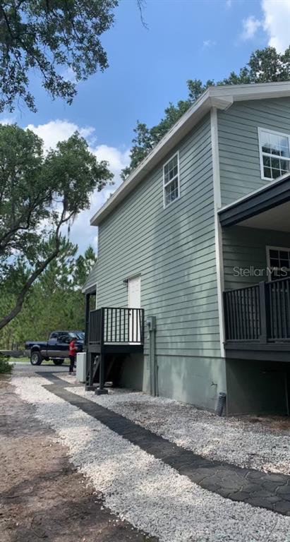 The exterior side of a light green house features a small deck and gravel landscaping — 7152 SANDY LANE, WESLEY CHAPEL, FL