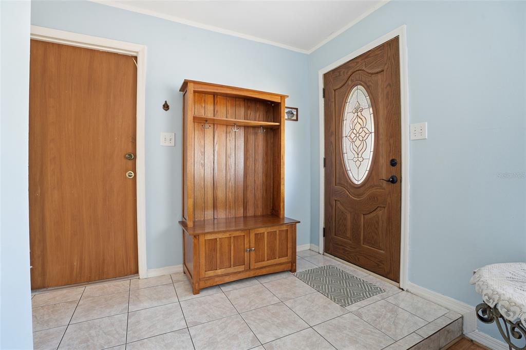 An entryway features light blue walls, tiled flooring, a wooden hall tree, and two doors — 7002 CRESTLAKE DRIVE, ORLANDO, FL