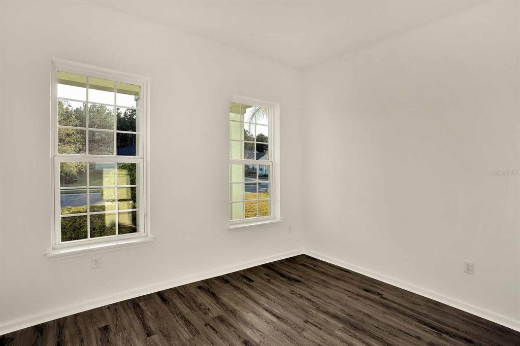 An empty room features white walls, dark wood-look flooring, and two windows — 32 WINTERFIELD PLACE, ST AUGUSTINE, FL