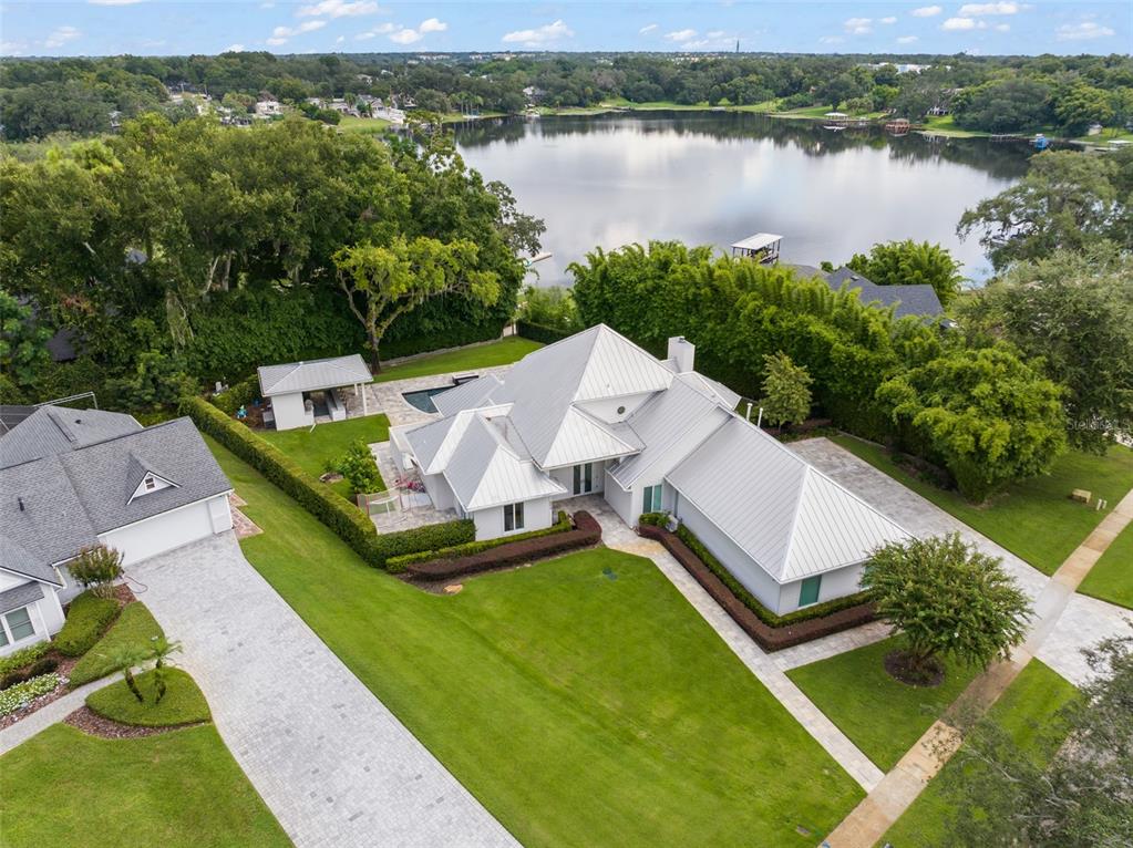 An aerial view shows a white house with a metal roof, pool, and lakefront backyard — 9019 SPENCE COURT, GOTHA, FL