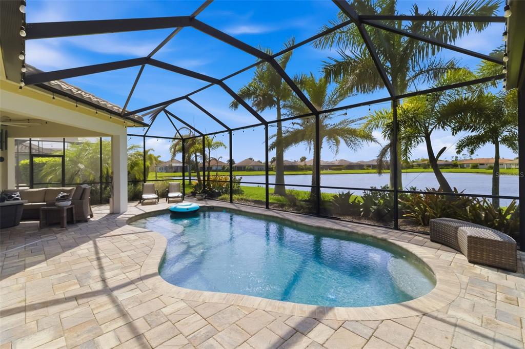 A screened-in patio features a swimming pool, paver deck, and views of a lake — 10107 CARNOUSTIE PLACE, BRADENTON, FL