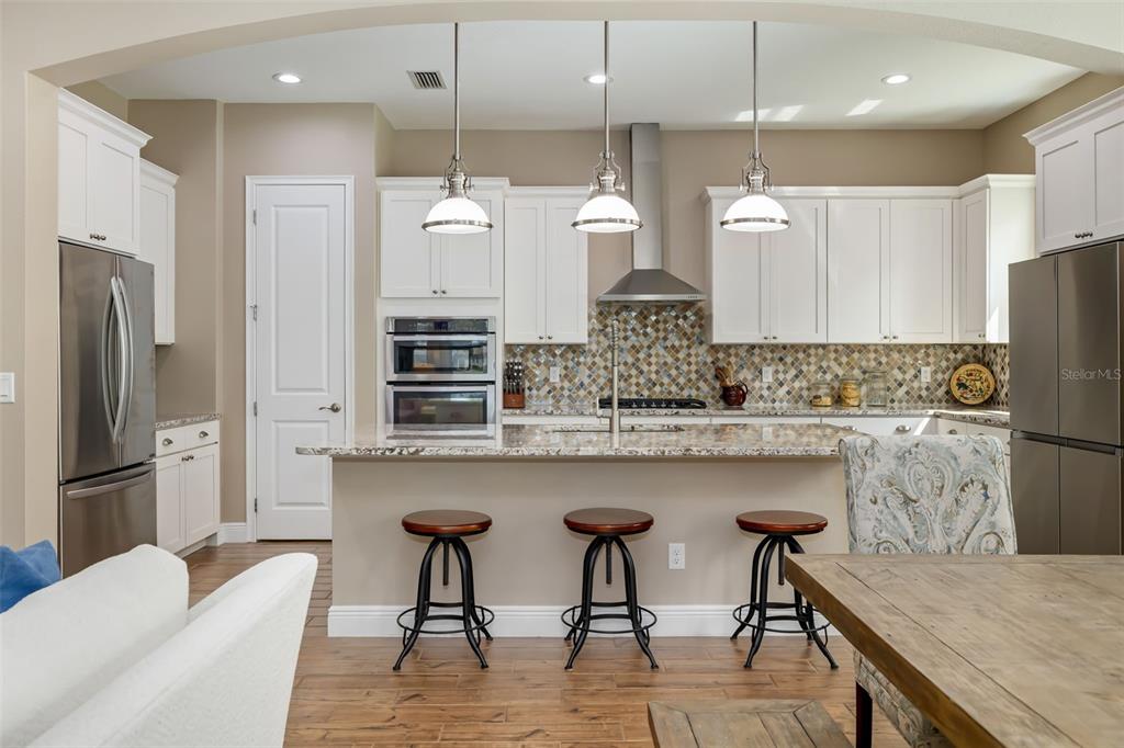 A kitchen features white cabinets, stainless steel appliances, a granite island, and three bar stools — 10107 CARNOUSTIE PLACE, BRADENTON, FL