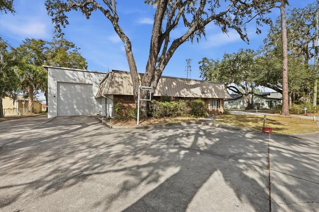 A commercial building with a roll-up garage door, tan mansard roof, and large oak trees — 1022 WILFRED DRIVE UNIT SEALED BID!, ORLANDO, FL