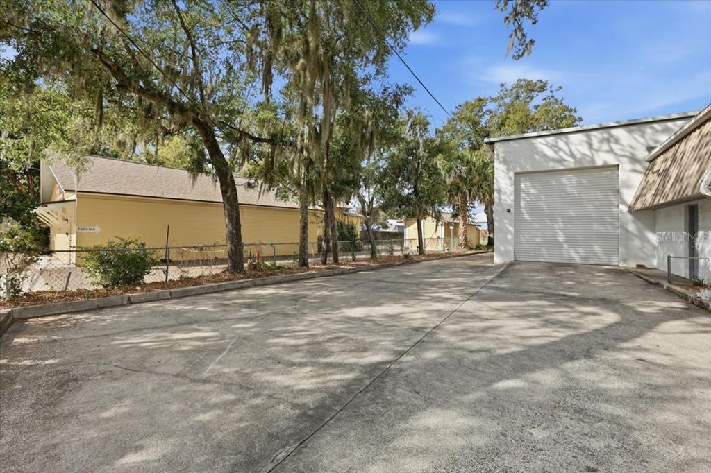 A paved driveway leads to a white industrial building with a large roll-up garage door — 1022 WILFRED DRIVE UNIT SEALED BID!, ORLANDO, FL