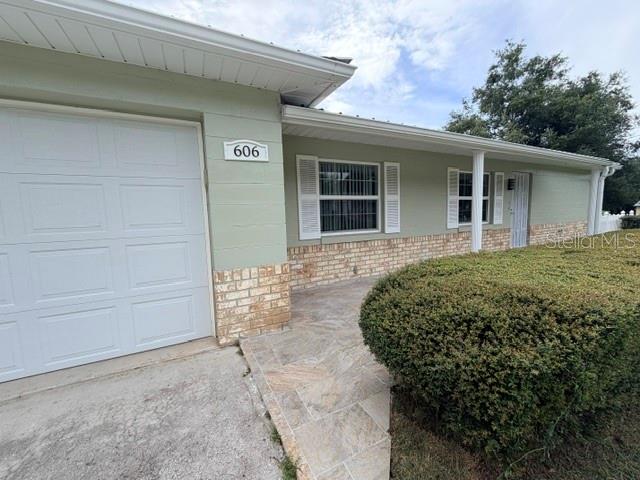 A light green house exterior features a white garage door, stone accents, and a hedge — 606 SECOND AVENUE, LADY LAKE, FL