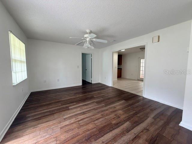 A living room with dark wood-look flooring, a ceiling fan, and an adjacent tiled kitchen — 606 SECOND AVENUE, LADY LAKE, FL