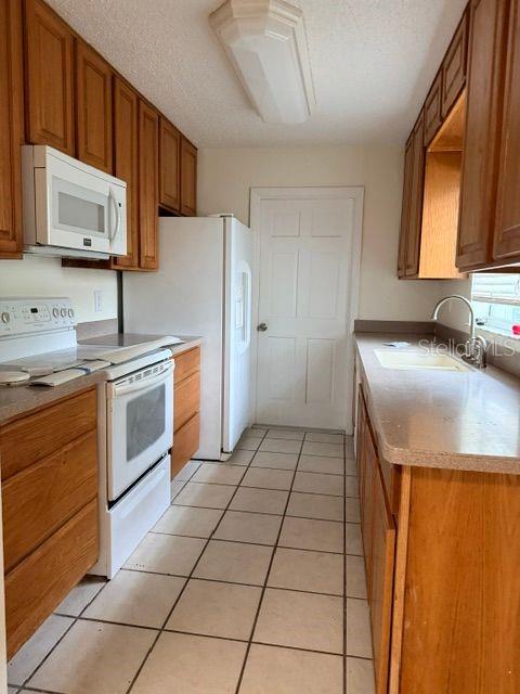 A kitchen features oak cabinets, white appliances, a tiled floor, and a white door — 606 SECOND AVENUE, LADY LAKE, FL