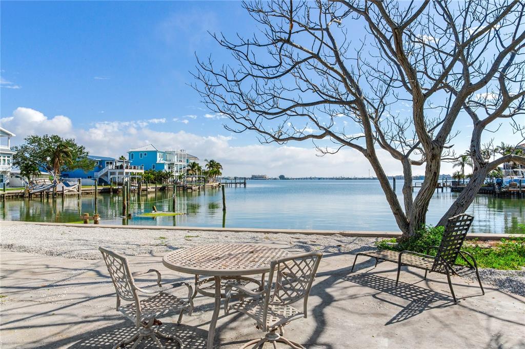 A patio with metal furniture overlooks a calm bay with houses and a large tree — 409 161ST AVENUE, REDINGTON BEACH, FL