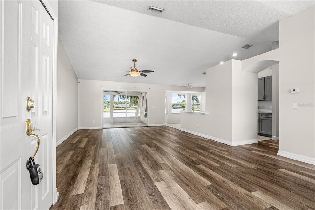 An open-concept living area features wood-look flooring, a vaulted ceiling, and views of a lake — 1730 ARASH CIRCLE, PORT ORANGE, FL