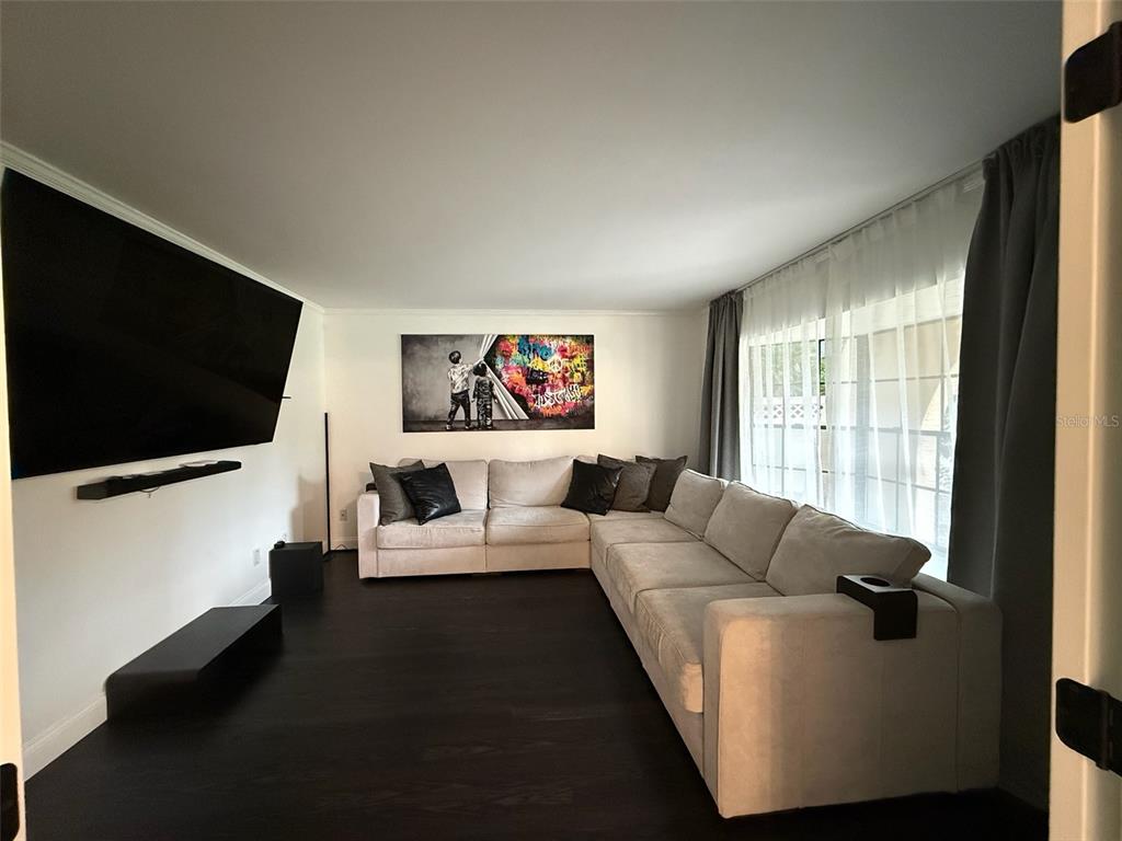A living room features a large sectional sofa, a wall-mounted television, and dark wood flooring — 8004 BELTREES COURT, TEMPLE TERRACE, FL