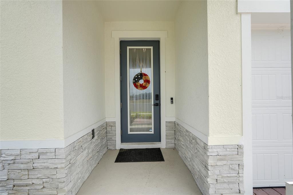 A covered entryway features a gray front door with a glass insert and stone siding — 9844 PINE MILL COURT, CLERMONT, FL