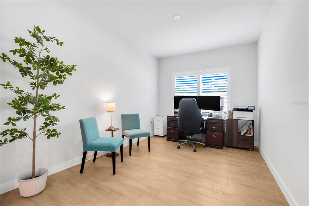 A home office features light wood-look tile flooring, a desk with dual monitors, and two chairs — 9844 PINE MILL COURT, CLERMONT, FL