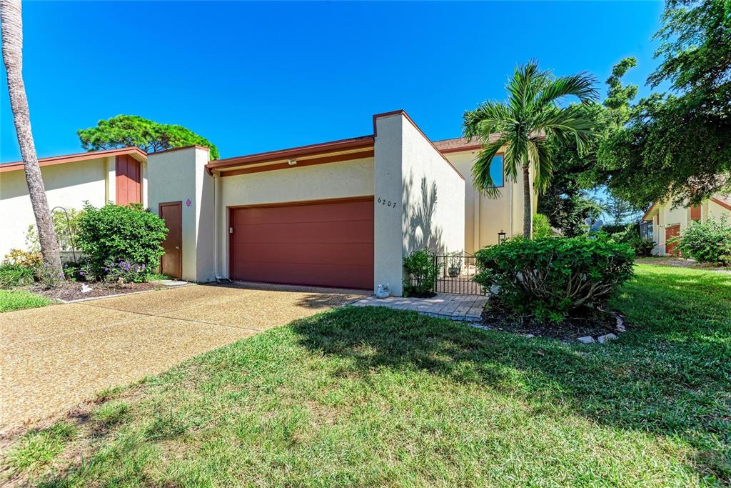 A single-story house with a brown garage door, light-colored stucco walls, and a palm tree — 6207 COURTSIDE DRIVE UNIT 23, BRADENTON, FL