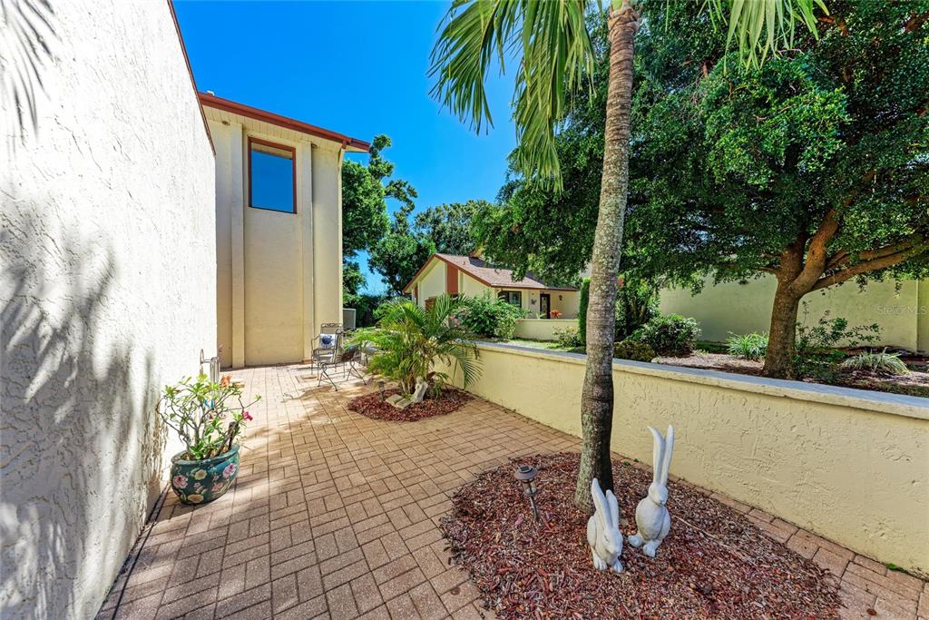 A paved patio area features a palm tree, two rabbit statues, and a low wall — 6207 COURTSIDE DRIVE UNIT 23, BRADENTON, FL