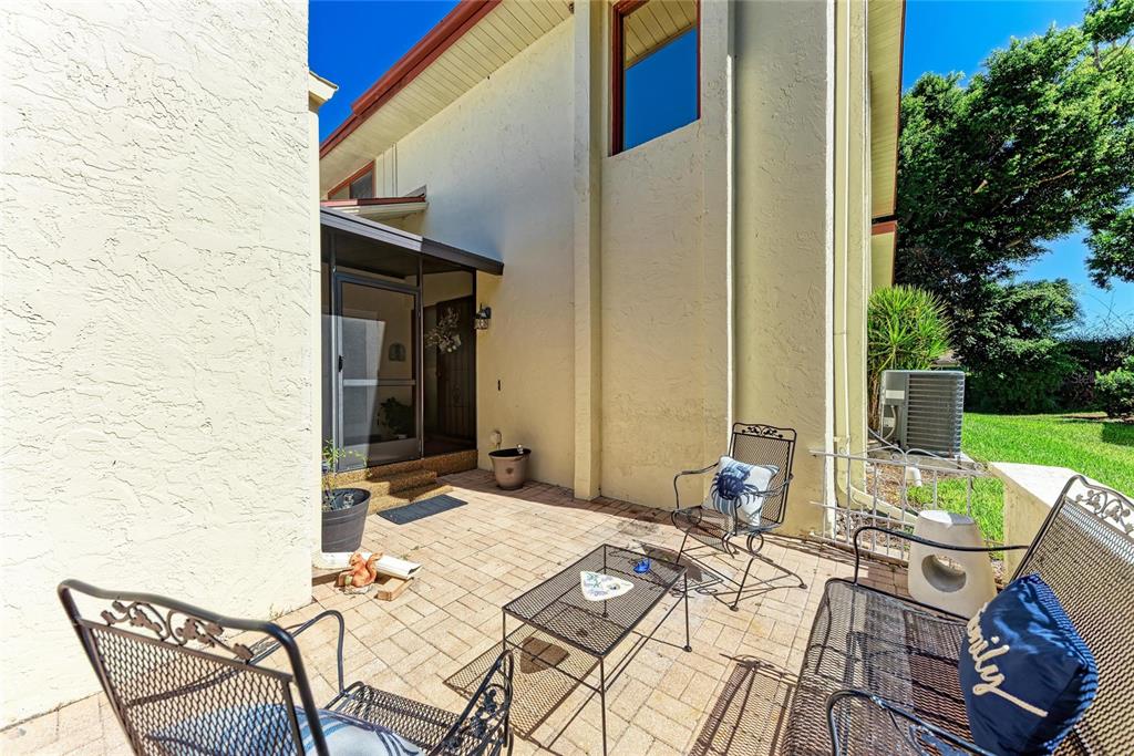 A paved patio features metal outdoor furniture and a screened entryway against a stucco house — 6207 COURTSIDE DRIVE UNIT 23, BRADENTON, FL