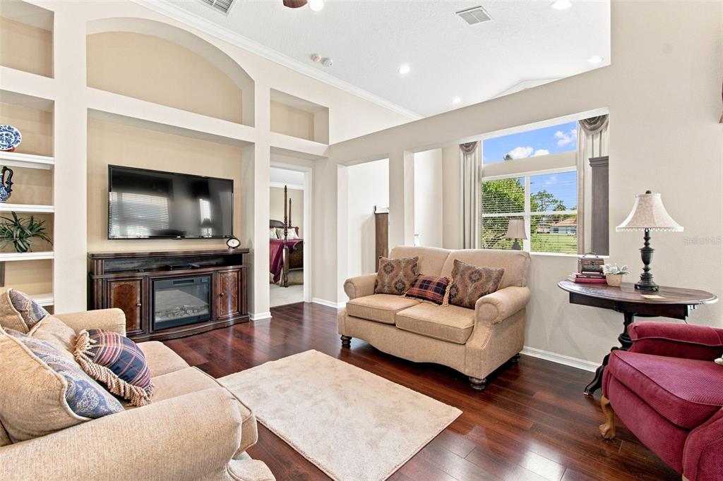 A living room with hardwood floors, a beige sofa, a red armchair, and large windows — 23737 ESTERO COURT, LAND O LAKES, FL