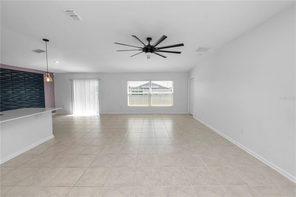A spacious, tiled living area features a ceiling fan, a kitchen island, and sliding doors — 1431 LASSEN STREET, HAINES CITY, FL