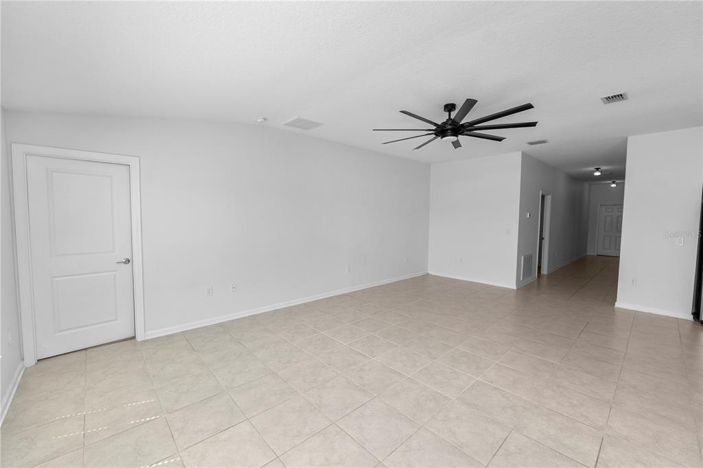 An empty room with light-colored tile flooring, white walls, and a black ceiling fan — 1431 LASSEN STREET, HAINES CITY, FL
