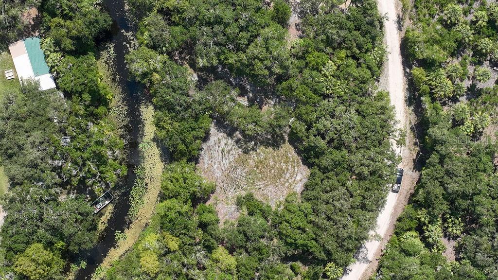 An aerial view shows a wooded lot with a dirt road, a canal, and a building — 7096 E CHANNEL DRIVE, HERNANDO, FL