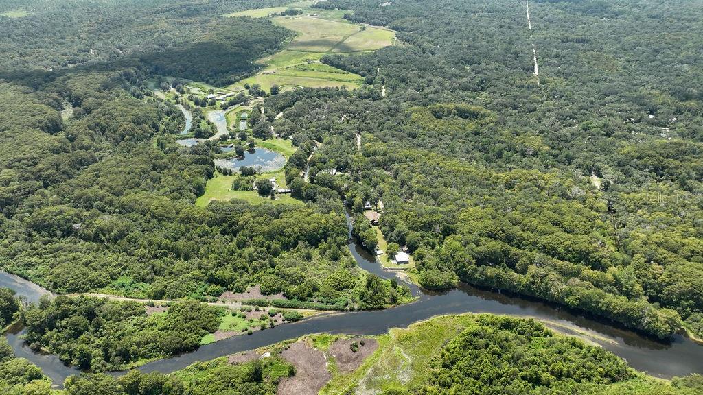 An aerial view shows a winding river flowing through a dense forest with scattered buildings — 7096 E CHANNEL DRIVE, HERNANDO, FL