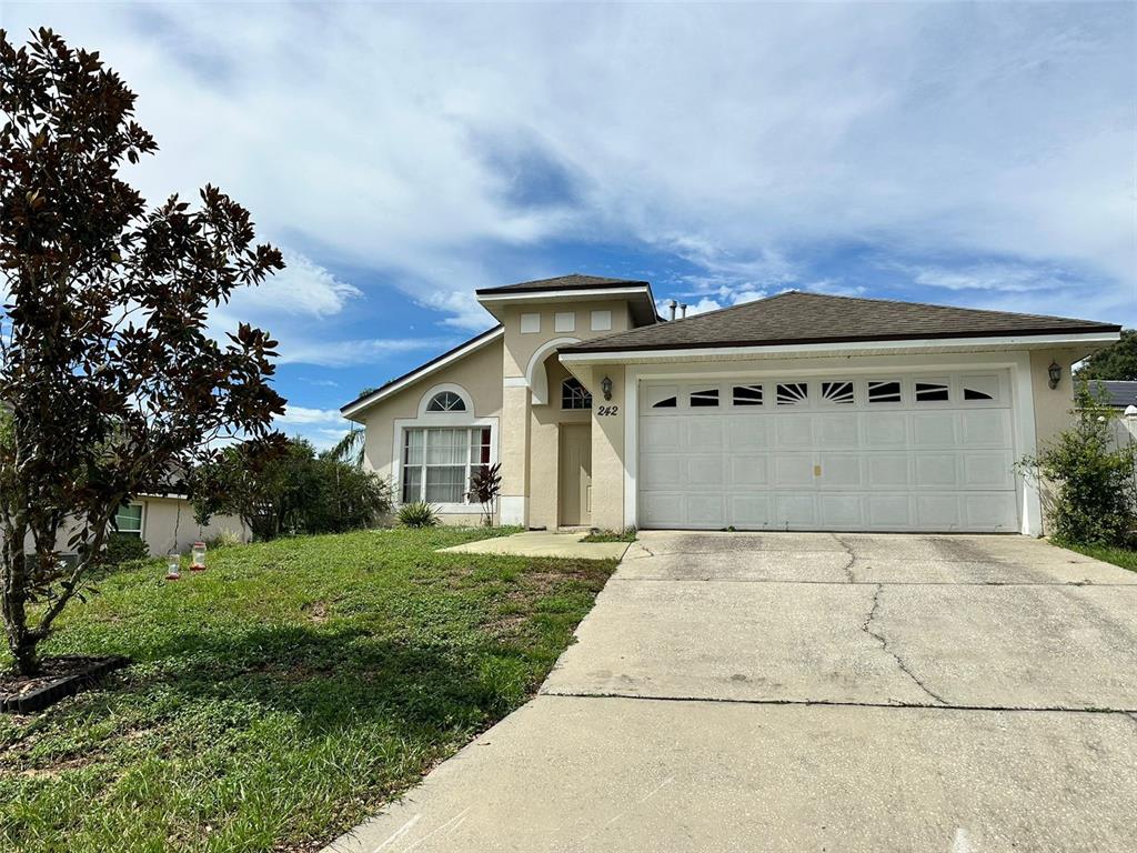 A single-story house with a beige stucco exterior, a two-car garage, and a concrete driveway — 242 DURANGO LOOP STREET, DAVENPORT, FL