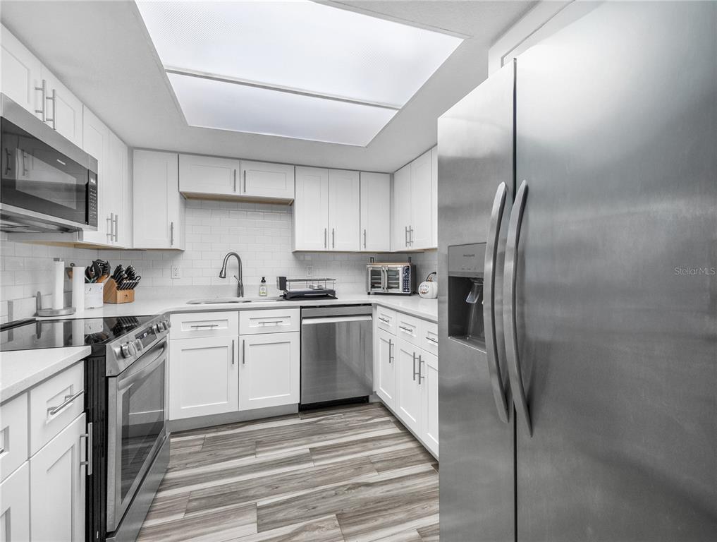 A modern kitchen features white cabinets, stainless steel appliances, and wood-look flooring — 622 FAIRWAYS CIRCLE UNIT A, OCALA, FL