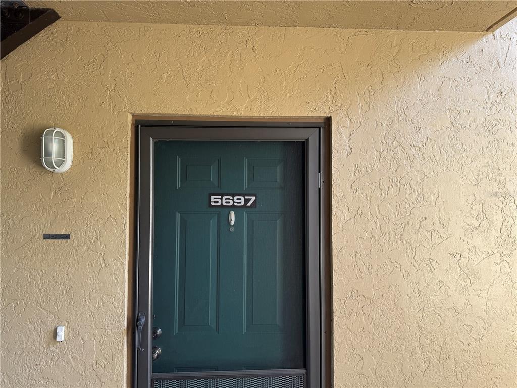 A dark green front door with the number 5697 is set into a textured beige wall — 5697 ASHTON LAKE DRIVE UNIT 6, SARASOTA, FL
