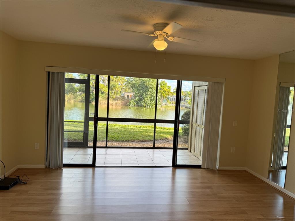 A living room with light wood flooring, a ceiling fan, and sliding doors opening to a lake — 5697 ASHTON LAKE DRIVE UNIT 6, SARASOTA, FL