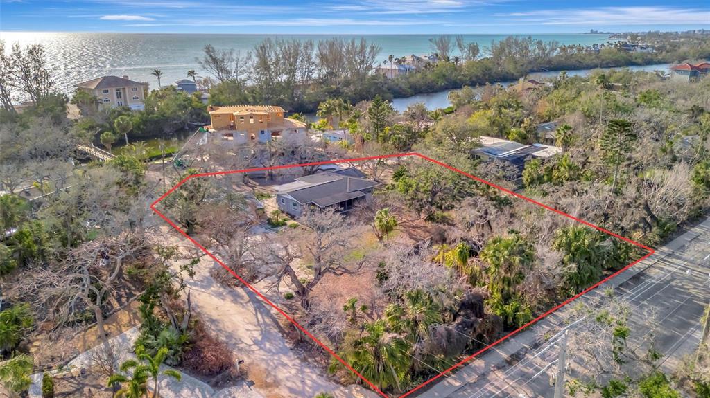 An aerial view shows a house on a large, tree-filled lot near the ocean — 8555 HERON LAGOON CIRCLE, SARASOTA, FL