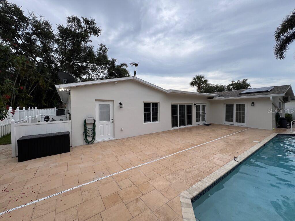 A backyard patio with light-colored pavers features a swimming pool and a white house exterior — 146 GIRALDA BOULEVARD NE, ST PETERSBURG, FL