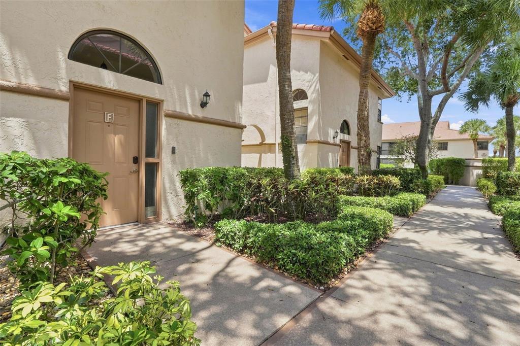A sidewalk leads to the entrance of a tan stucco building with a letter F — 5196 EUROPA DRIVE UNIT F, BOYNTON BEACH, FL
