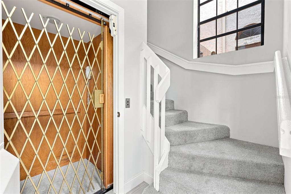 A residential elevator with a gold metal gate stands beside a carpeted staircase — 5196 EUROPA DRIVE UNIT F, BOYNTON BEACH, FL