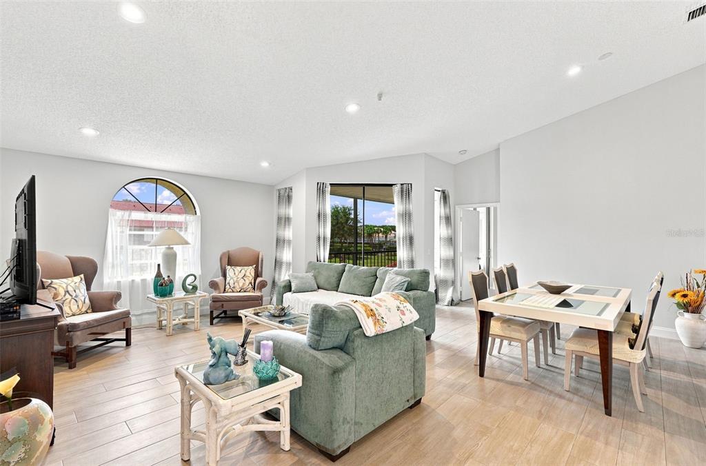 A living and dining area features light wood-look tile flooring, neutral walls, and large windows — 5196 EUROPA DRIVE UNIT F, BOYNTON BEACH, FL