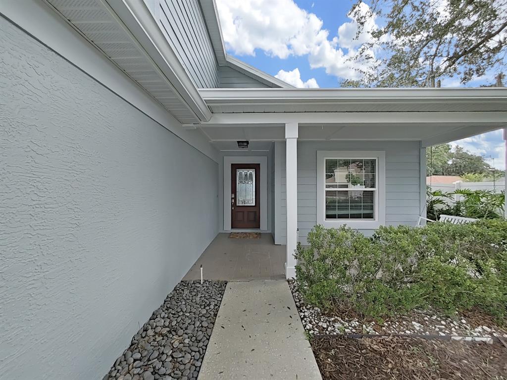 A light blue house exterior features a covered entryway, a brown front door, and landscaping — 2348 ASAPH COURT, LAND O LAKES, FL