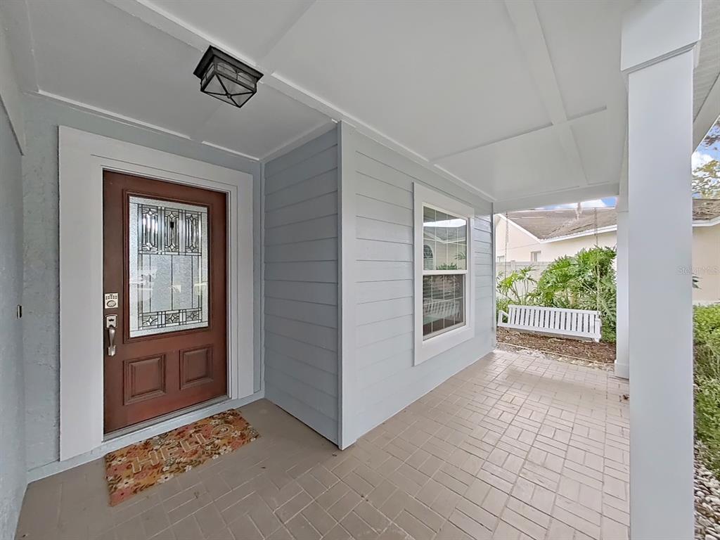 A covered front porch features a brown door with a decorative glass insert and a swing — 2348 ASAPH COURT, LAND O LAKES, FL