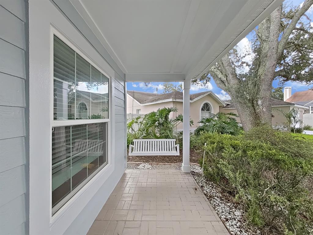A covered front porch features light-colored pavers, a white hanging bench, and gray siding — 2348 ASAPH COURT, LAND O LAKES, FL
