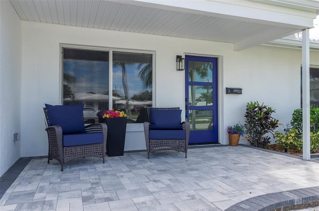 A covered patio features gray pavers, two wicker chairs with blue cushions, and a blue door — 4034 MAINLANDS BOULEVARD N, PINELLAS PARK, FL