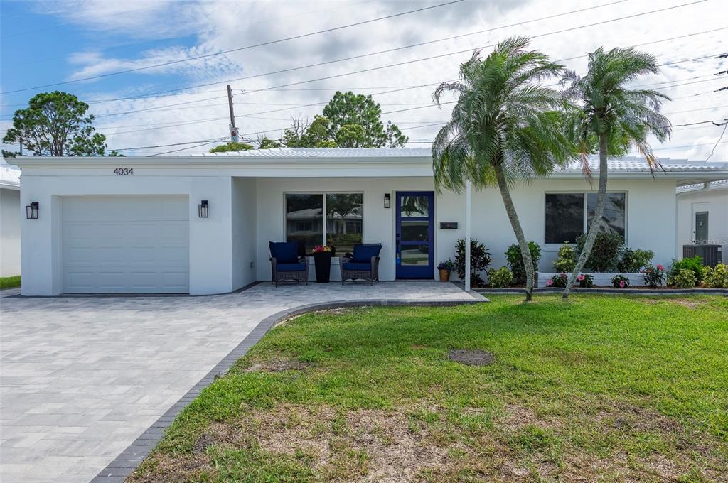 A white single-story house features a paved driveway, a blue front door, and two palm trees — 4034 MAINLANDS BOULEVARD N, PINELLAS PARK, FL