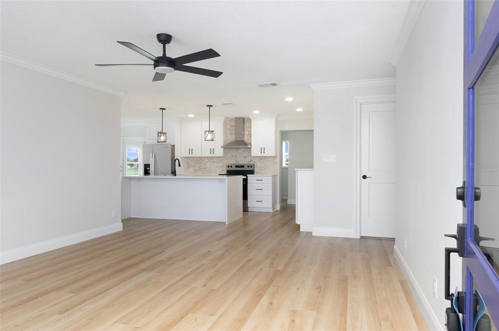 A bright, open-concept kitchen and living area featuring light wood flooring and white cabinetry — 4034 MAINLANDS BOULEVARD N, PINELLAS PARK, FL