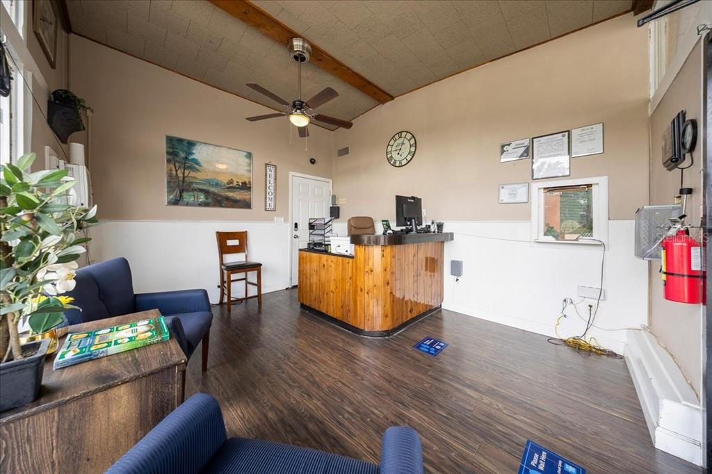 A reception area features a wooden desk, blue armchairs, wood-look flooring, and a ceiling fan — 2210 S PINE AVENUE, OCALA, FL