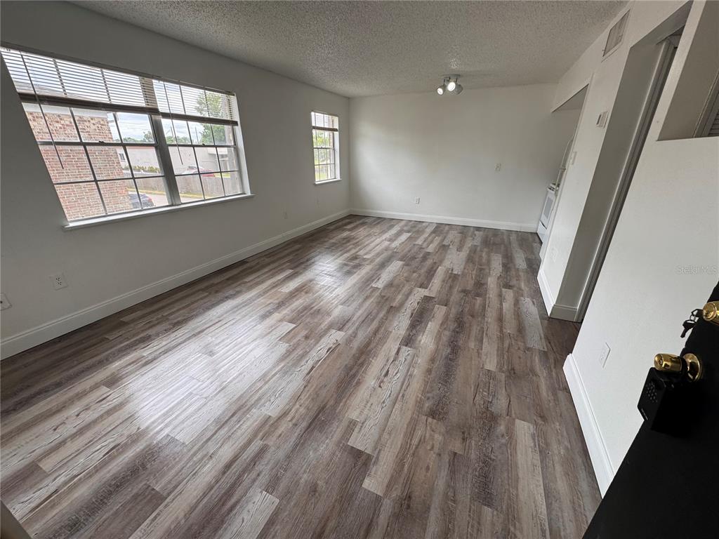 An open-concept living area features wood-look flooring, a small kitchen, and a black entry door — 5317 CURRY FORD ROAD UNIT O201, ORLANDO, FL
