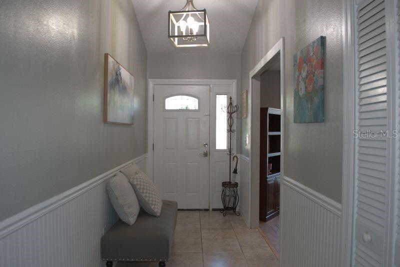 An entryway features a gray bench, beadboard wainscoting, a light fixture, and a white front door — 3486 HAWKIN DRIVE, KISSIMMEE, FL