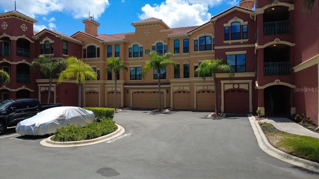 Exterior view of a multi-story apartment complex with several garage doors and palm trees — 2757 VIA CIPRIANI UNIT 1131B, CLEARWATER, FL