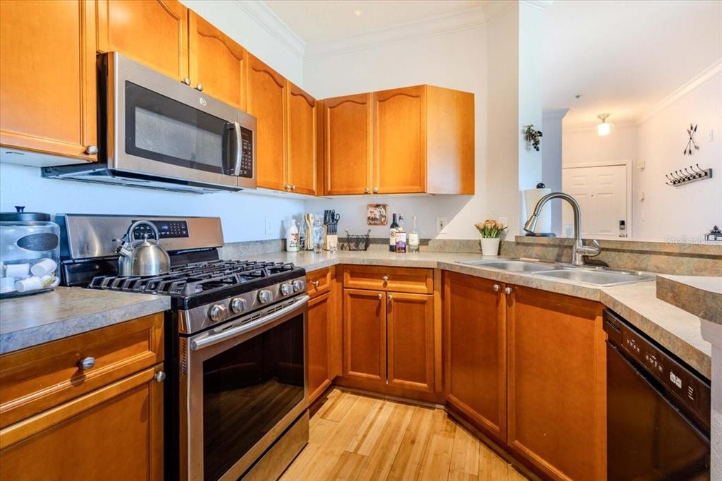 A kitchen features wood cabinets, stainless steel appliances, and a double sink with a faucet — 2757 VIA CIPRIANI UNIT 1131B, CLEARWATER, FL