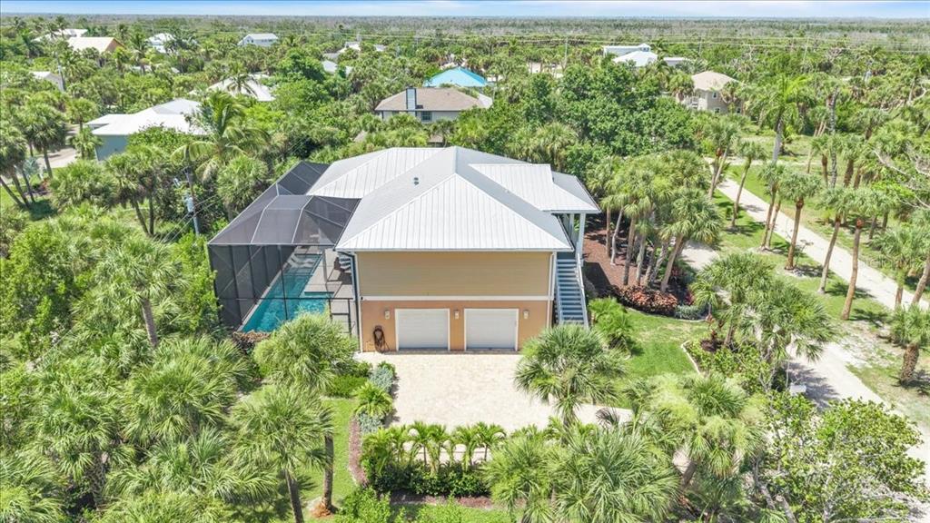 An aerial view of a two-story house with a metal roof, garage, and screened pool — 9277 BELDING DRIVE, SANIBEL, FL