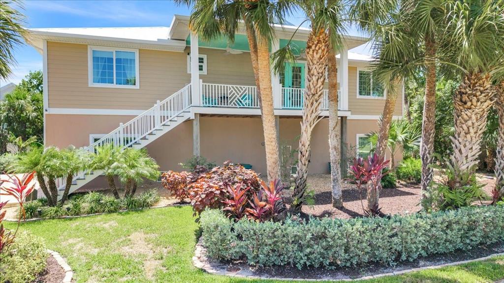 A two-story house with tan siding, a white staircase, and a covered porch with palm trees — 9277 BELDING DRIVE, SANIBEL, FL