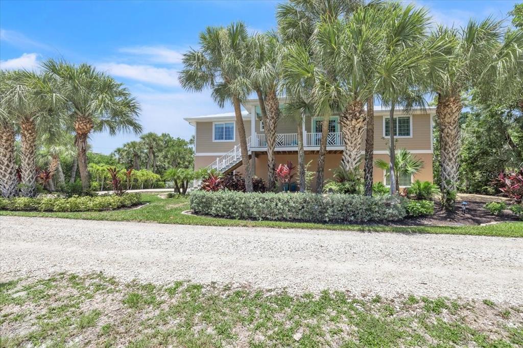 A two-story house with a raised deck and stairs surrounded by palm trees and landscaping — 9277 BELDING DRIVE, SANIBEL, FL