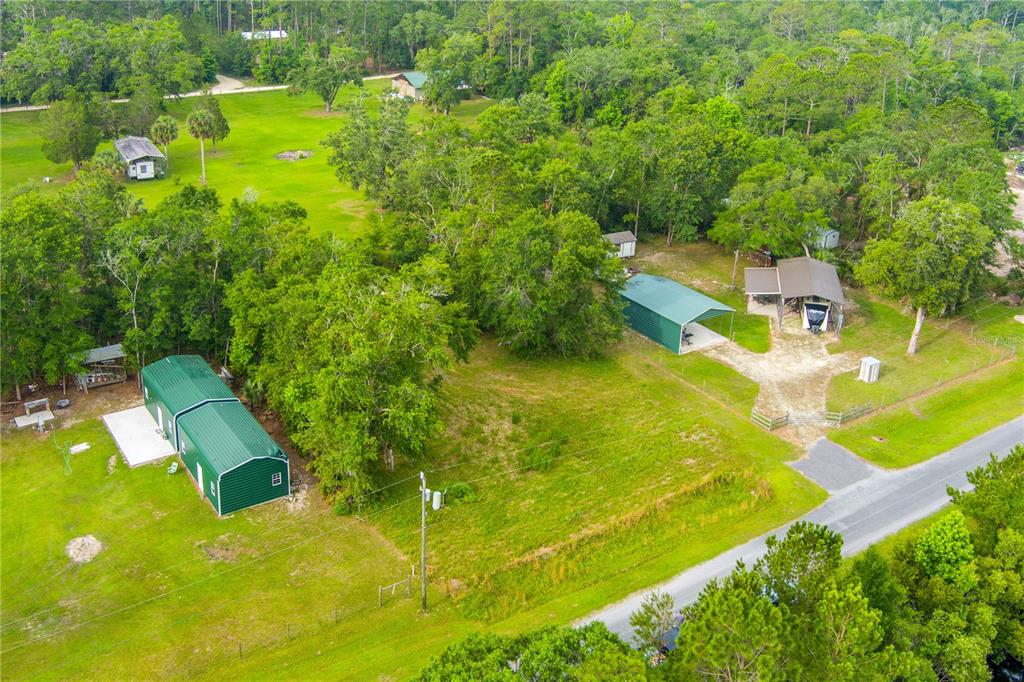 An aerial view shows a rural property with several metal outbuildings, green lawns, and trees — 400 COASTAL OAK LANE NW, STEINHATCHEE, FL