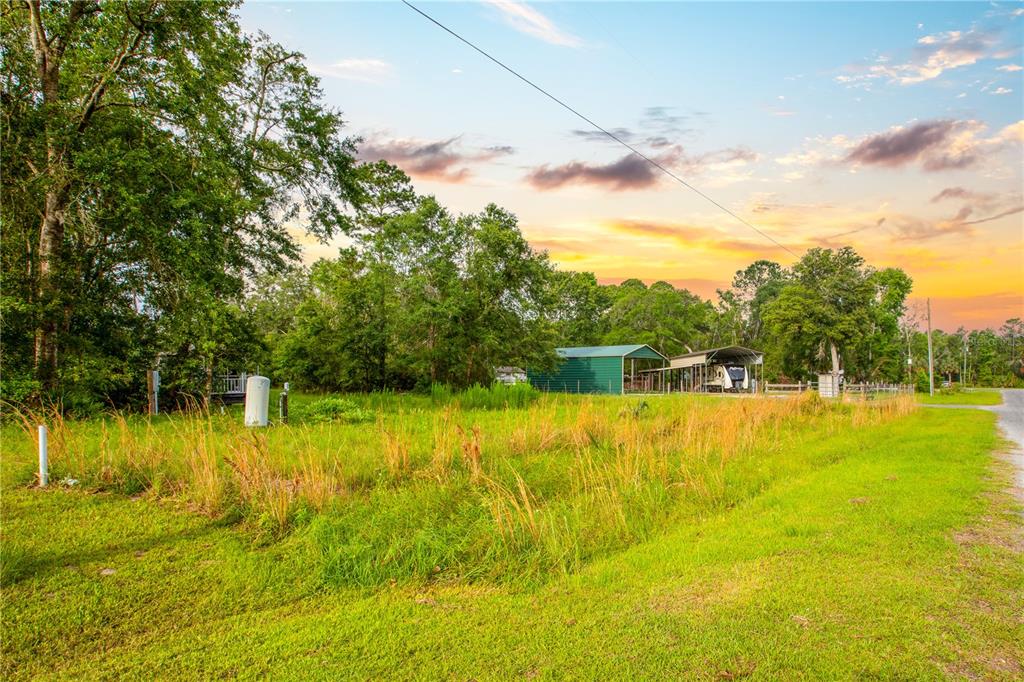 A grassy vacant lot features a green metal storage building and a covered RV shelter — 400 COASTAL OAK LANE NW, STEINHATCHEE, FL